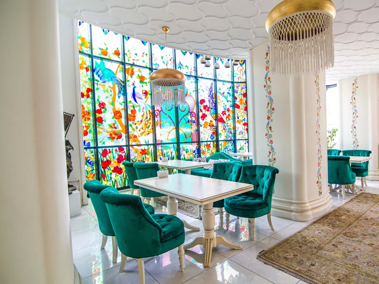 Restaurant interior with green velvet chairs, colourful stained-glass windows and gold pendant lights