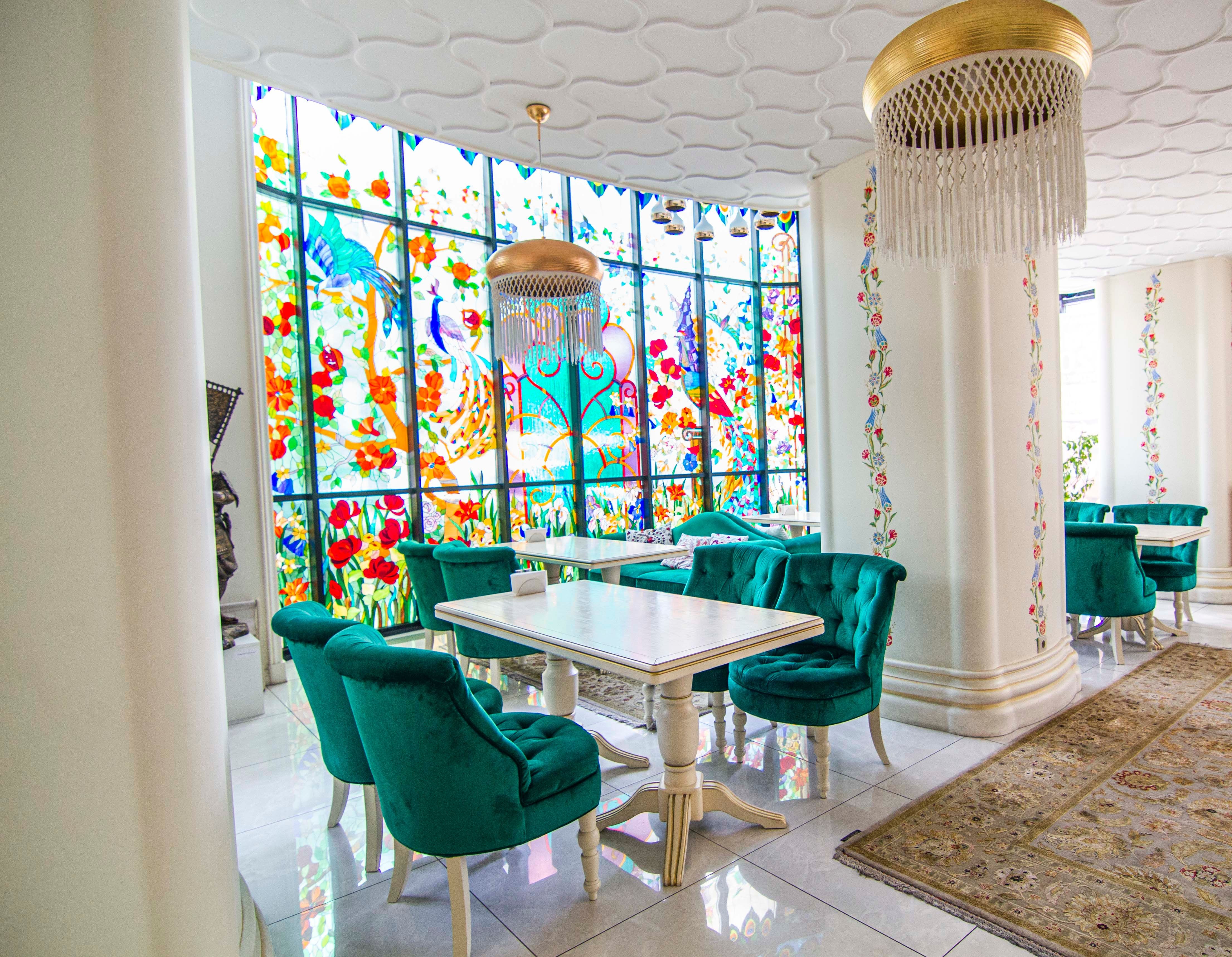 Restaurant interior with green velvet chairs, colourful stained-glass windows and gold pendant lights