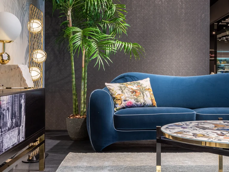 Interior with a blue velvet sofa, patterned cushion, tall palm and decorative globe lighting