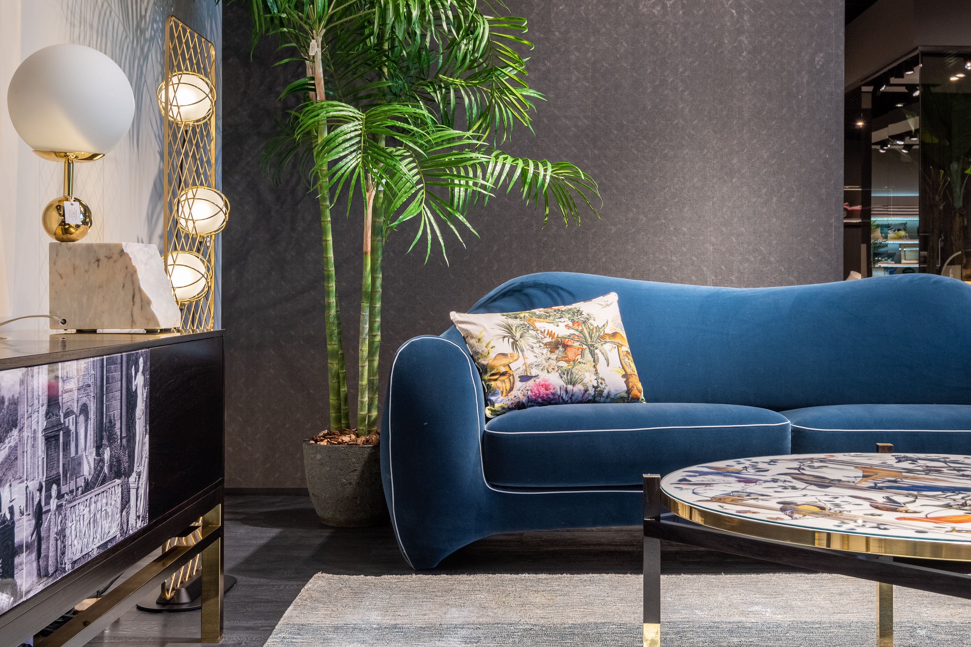 Interior with a blue velvet sofa, patterned cushion, tall palm and decorative globe lighting
